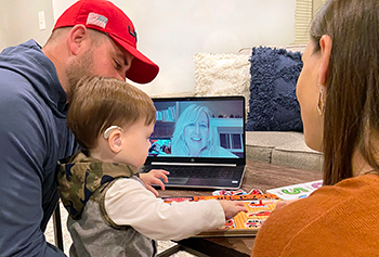 a telehealth session, the child, mother, and father communicating with a health professional on their laptop